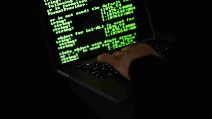 Silhouette of a hacker typing on a laptop in the dark with green code on screen., tags: cybercrime-forum - pexel